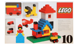Early LEGO set showing a simple brick-built house and small vehicles, demonstrating the basic design style of early LEGO toys.